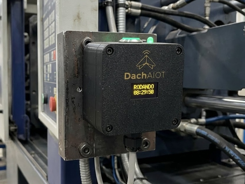 Botoeira Inteligente Wi-Fi da Dach AIOT fixada na lateral de uma injetora no chão de fábrica, com o display mostrando a máquina rodando